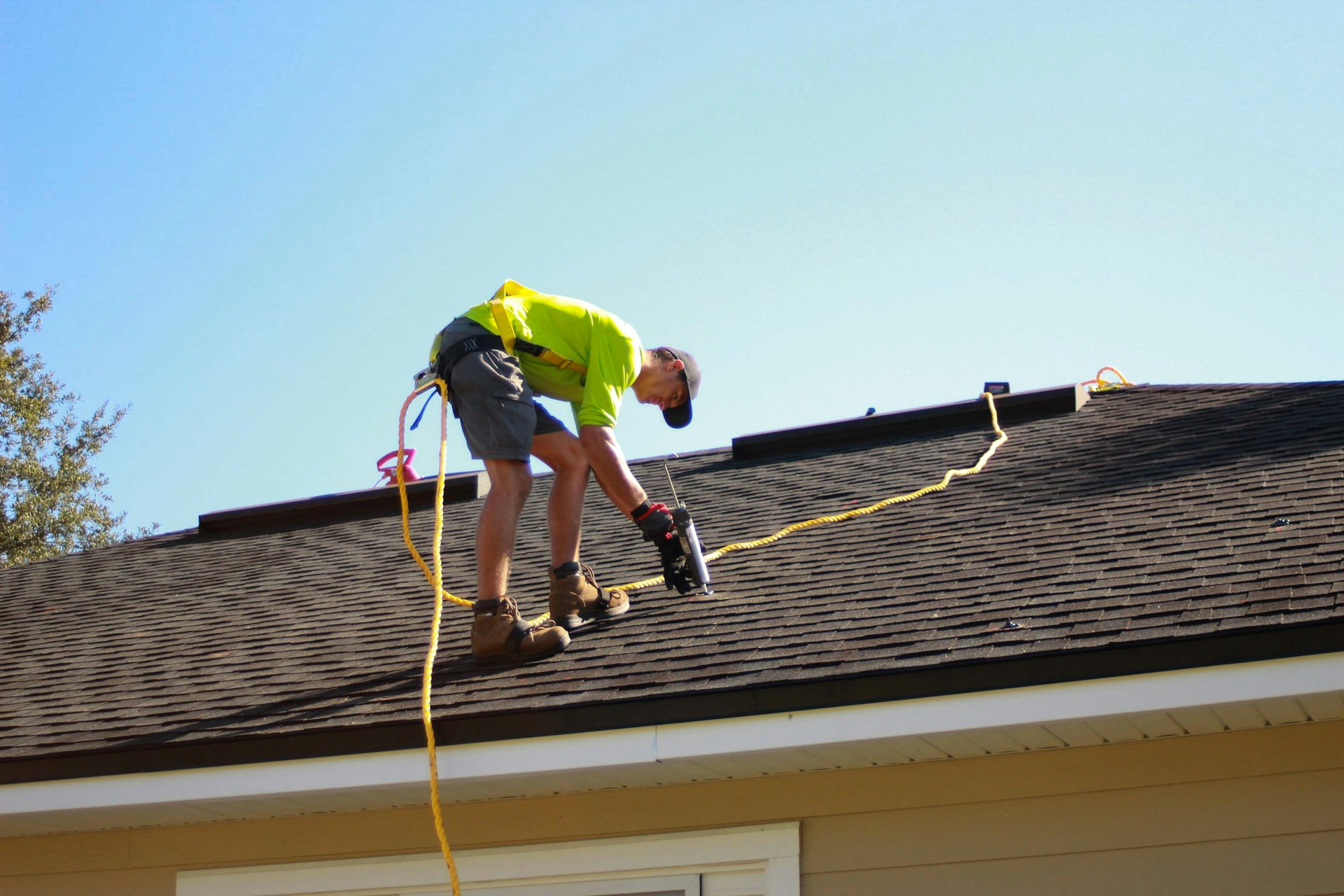 A roofer fastening shingles on a residential roof against a clear sky
