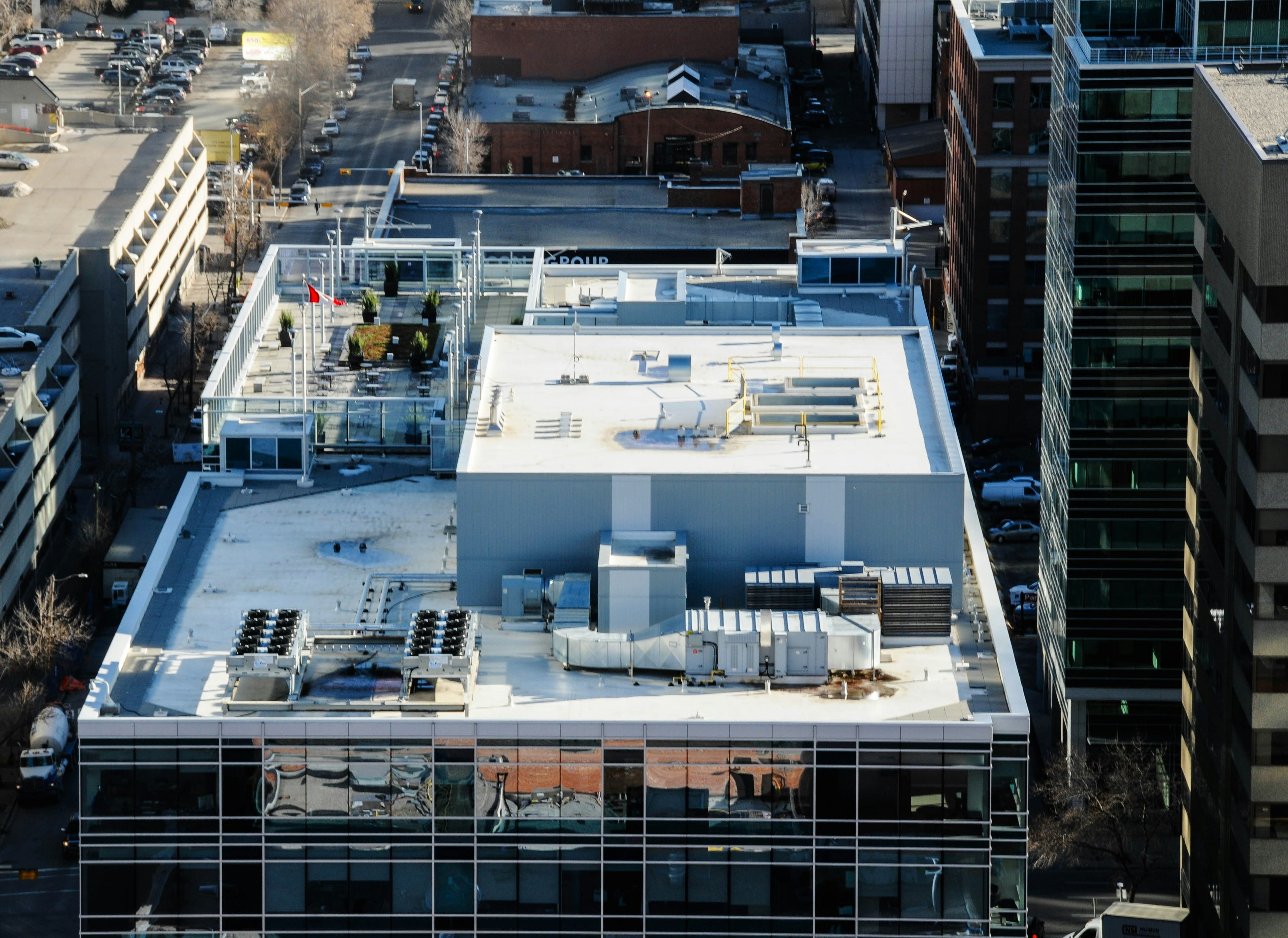 Aerial view of a white membrane commercial roof with rooftop units, surrounded by city buildings
