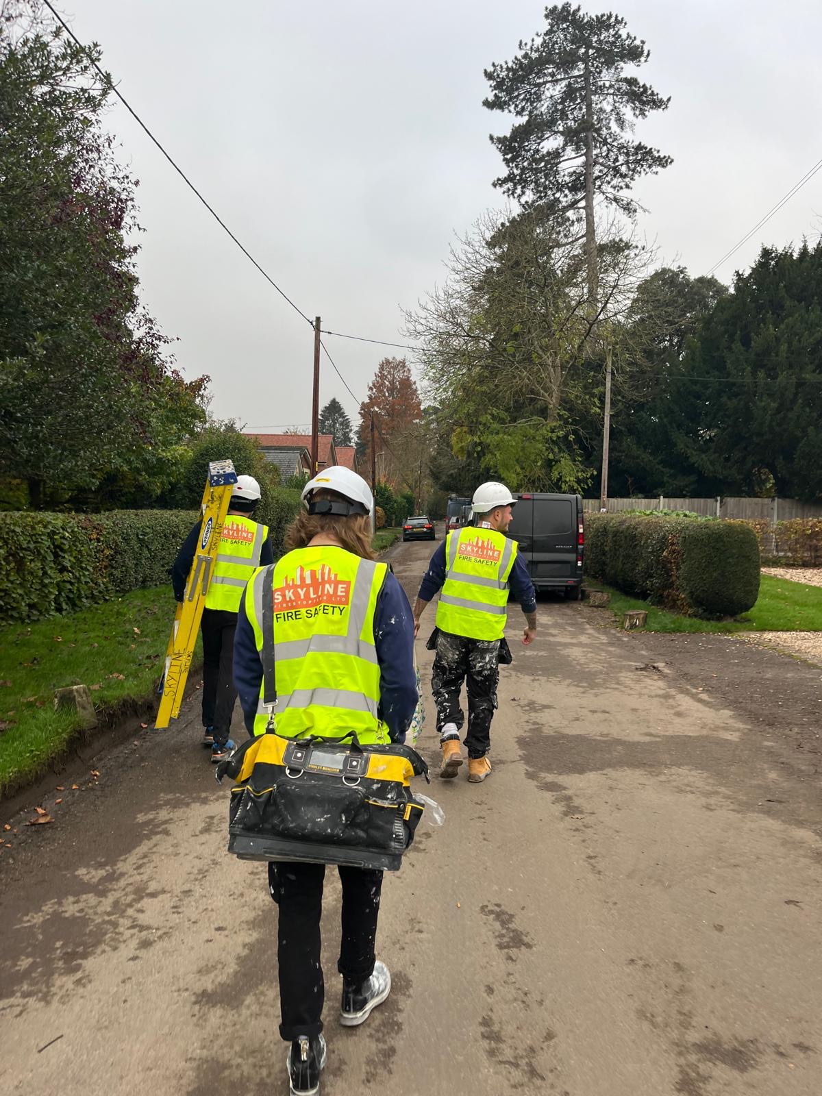 Skyline installers in branded hi-vis walking to a job with ladder and tool bags