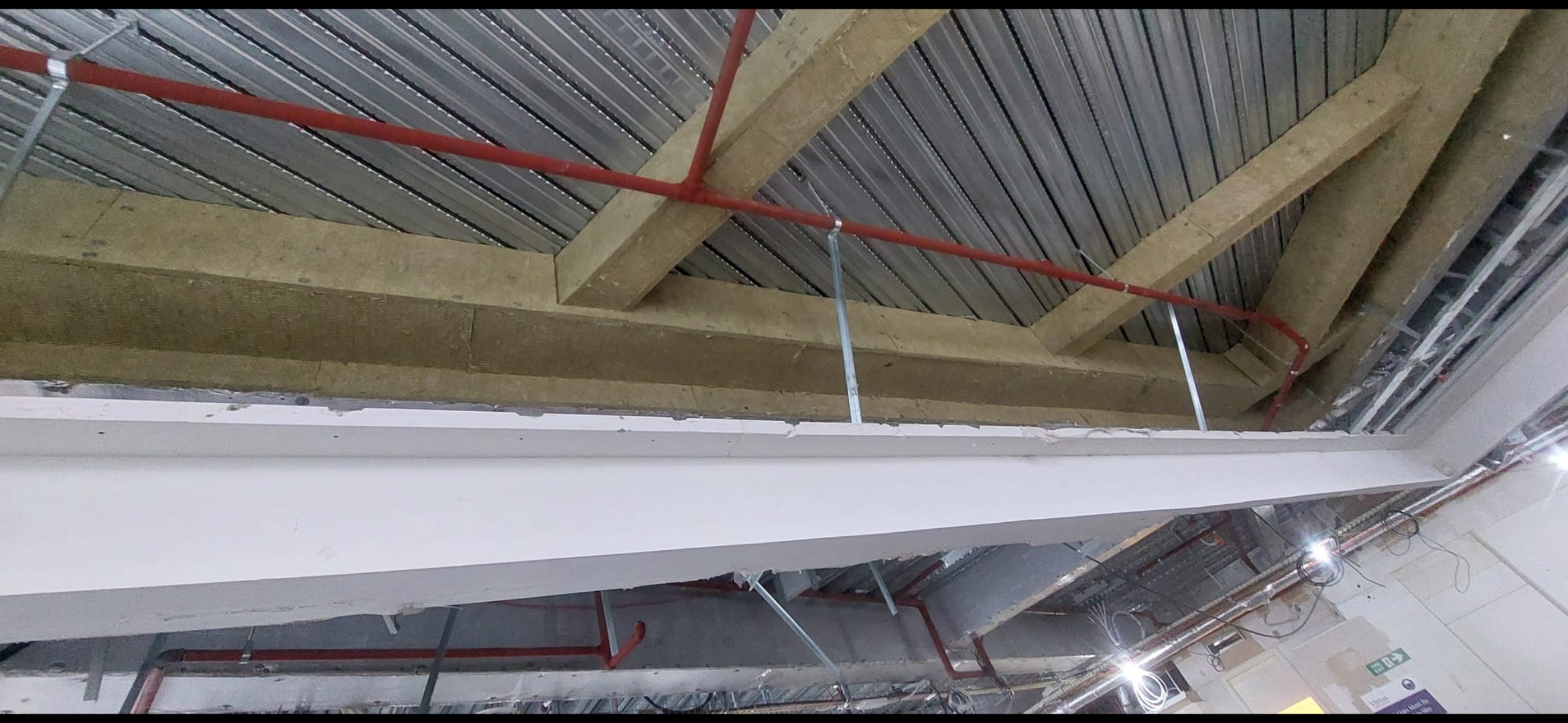 Structural steel ceiling beam protected with intumescent paint, with red sprinkler pipes and a metal deck soffit above.