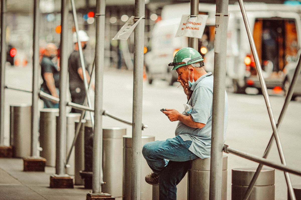 A trade worker in a hard hat checking his phone beside scaffolding on a city job